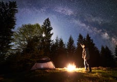 野营在旅游帐篷附近的男性远足者enjoyng夜在营火在蓝色满天星斗的天空和银河下 库存图片 野营在旅游帐篷附近的男性远足者enjoyng夜在营火在蓝色满天星斗的天空和银河下 库存图片