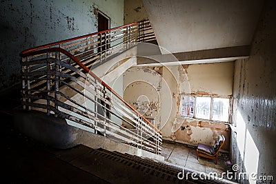 Abandoned building creepy dark moody staircase in dilapidated run down old deserted hospital school ruin with a single empty chair Stock Photo