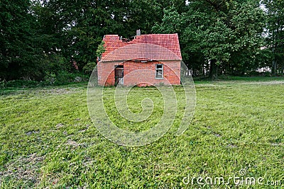 Abandoned damaged brick shed behind a green meadow Stock Photo