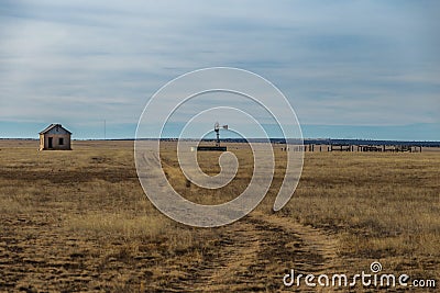 Abandoned homefront with windmill and wooden fencing in yellow grass pasture Stock Photo