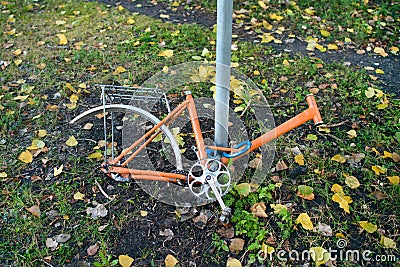 Abandoned old bicycle without wheels, chained to metal pole with blue locker. Stock Photo