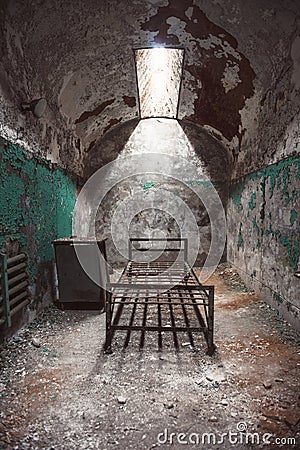 Abandoned prison cell room with old rusty bed frame and peeling walls Stock Photo