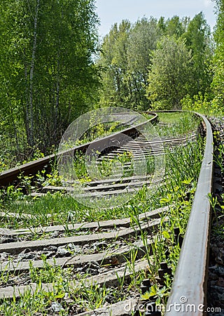 Abandoned railroad overgrown with grass and winding among trees Stock Photo