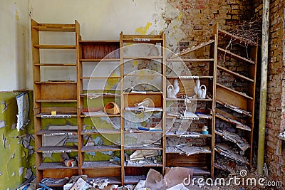 An abandoned room with a wooden bookshelf filled with old books and objects, and a crumbling brick wall. Old shelves for papers in Stock Photo
