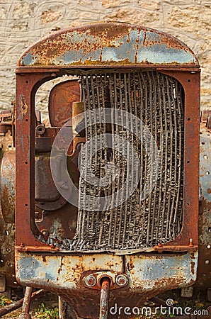 Abandoned rusty wheeled tractor against the background of a gray stone wall. View of destroyed radiator Stock Photo