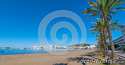 Abandoned sailboat on the beach. Rows of palm trees line water`s edge in Ibiza, St Antoni de Portmany Balearic Islands, Spain. Stock Photo