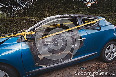An abandoned, stolen burnt out blue car parked on the sideway parking spotÐ± tied with yellow do not cross stripe Editorial Stock Photo