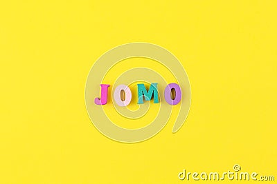 Abbreviation word JOMO in multicolored wooden letters on pastel yellow background. JOMO - Joy Of Missing Out. Opposition, choice, Stock Photo