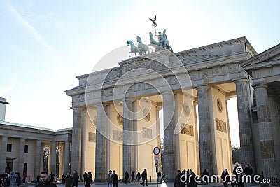 Above the Brandenburg Gate stands the Goddess of Victory in a chariot drawn by four horses heading towards the city. Editorial Stock Photo