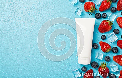 Above photo of berries strawberries blueberries transparent cubes ice water drops and white tube of cream isolated on the blue Stock Photo