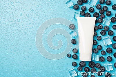 Above photo of blueberries transparent cubes ice water drops and white tube of cream isolated on the blue background with empty Stock Photo