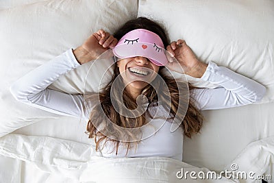 Happy millennial woman lying in bed with sleeping mask. Stock Photo