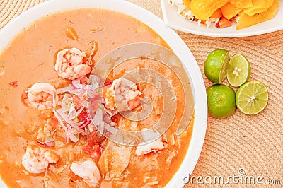 Above view of Ecuadorian food: shrimp cebiche with some chifles inside white bowl, lemon in a wooden table background Stock Photo