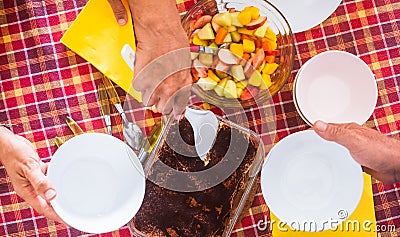 Group of people in the family share the moment of the homemade dessert and fresh fruit salad. Red checkered tablecloth. Tiramisu Stock Photo