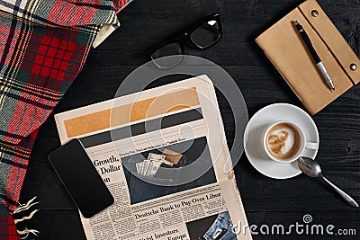 Above view of Smart phone, newspaper, scarf in a cage, glasses with notebook and cup of latte coffee on black wooden Stock Photo