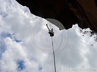 Abseiling a negative sanstone rock wall with blue sky on background - view from bellow Stock Photo