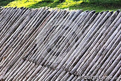 Abstract background of grey ancient wooden palisade of the protective fence on the green lawn. Stock Photo