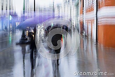 Abstract blurred people under the umbrellas. Rainy evening in the city street at autumn, blurred motion. Seasons Stock Photo