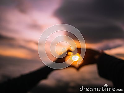 Abstract Blurred Photo of Silhouette Heart Hand sign with Sunrise Stock Photo