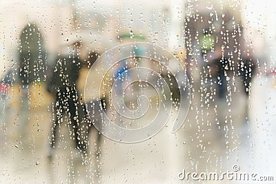 Abstract blurred silhouettes of people with umbrellas on rainy day in city, two persons seen through raindrops on window Stock Photo