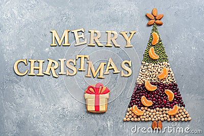 Abstract Christmas tree made from various legumes and almonds decorated with slices of mandarin on a gray background. The concept Stock Photo