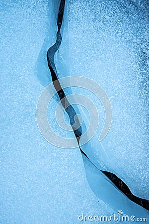 An abstract detailed vertical close up photograph of a crack or fault line in the blue frozen ice layer on a lake Stock Photo