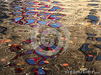 Abstract image of red windows of an old stone building reflected in the ripples of dark water with floating autumn leaves Stock Photo