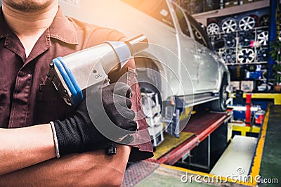 The abstract image of the technician holds an air wrench and blurred wheel alignment machine image is the backdrop. the concept of Stock Photo