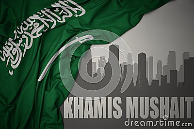 Abstract silhouette of the city with text Khamis Mushait near waving national flag of saudi arabia on a gray background Stock Photo