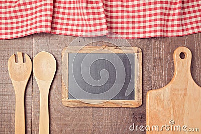 Abstract wooden background with red checked tablecloth, chalkboard and kitchen utensils. View from above Stock Photo