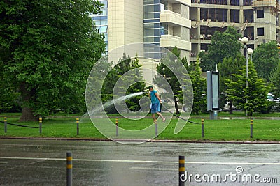 The person fulfills the obligations of the contract in any weather, even if it is absurd. Watering the city lawns in the rain Editorial Stock Photo