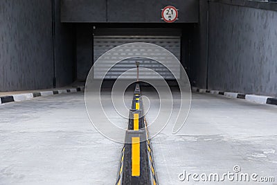 Access to underground car park with roller-shutter door and road dividers with yellow sticks Stock Photo