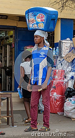 ACCRA,REPUBLIC OF GHANA - APRIL 30,2018:The young man sells ice cream. He holds the refrigerator with the goods on his head Editorial Stock Photo