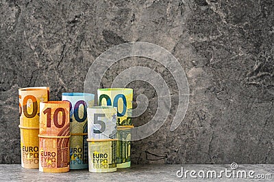 Accurately rolled hundred, fifty, twenty, ten and five paper euro banknotes on the grey stone background Stock Photo