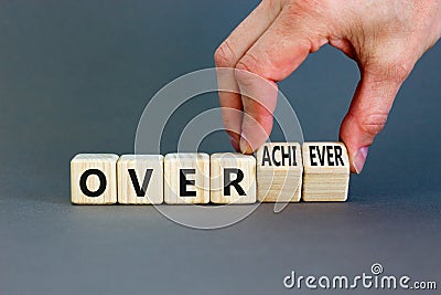 Achiever or overachiever symbol. Businessman turns wooden cubes and changes word Achiever to Overachiever. Beautiful grey table Stock Photo