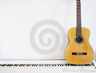 Acoustic guitar on piano keyboard in front of white wall Stock Photo