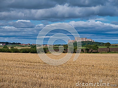 Across fields at harvest time, the imposing Bamburgh Castle dominates views from a dolerite outcrop in Northumberland, UK Editorial Stock Photo