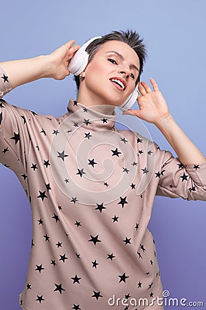 active bright caucasian young woman with a short haircut dressed in a beige suit listens to music in wireless bluetooth Stock Photo