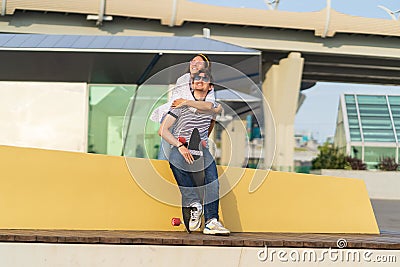 Carefree young couple has fun: girlfriend piggybacking boyfriend. Lovers girl and guy skateboarders Stock Photo