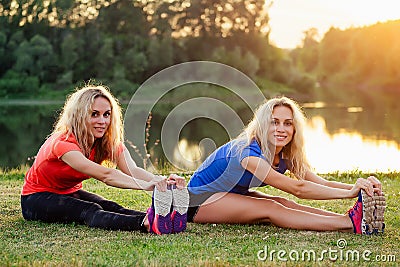 Active family at outdoor. two flexibility curly blonde woman twin sisters in stylish sportswear warm-up stretching full Stock Photo