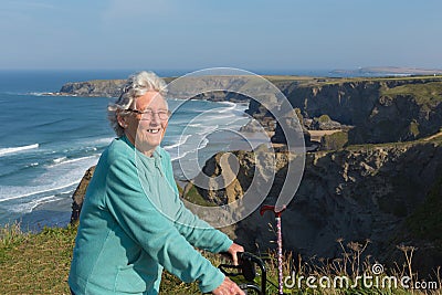 Active happy elderly female pensioner in eighties with mobility frame and walking stick by beautiful coast scene Stock Photo