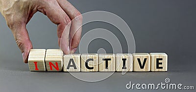 Active or inactive symbol. Businessman turns wooden cubes and changes the word Inactive to Active. Beautiful grey table grey Stock Photo