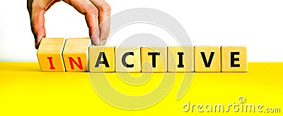 Active or inactive symbol. Businessman turns wooden cubes and changes the word Inactive to Active. Beautiful yellow table white Stock Photo