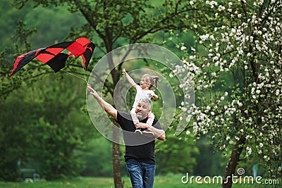 Active leisure. Running with red kite. Child sitting on the man`s shoulders. Having fun Stock Photo