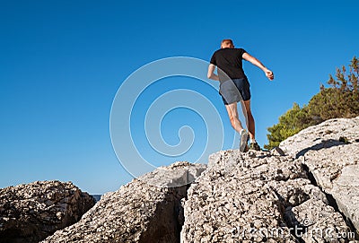 Active mountain skyrunner dressed black t-shirt and running shoes jogging the cliff summit during the morning scamper. Sporty Stock Photo