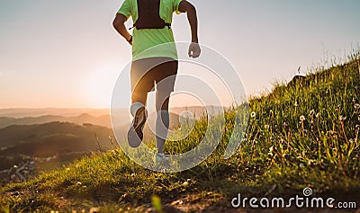 Active mountain trail runner dressed bright t-shirt with backpack running endurance marathon race by picturesque hills at sunset Stock Photo