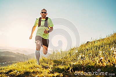 Active mountain trail runner dressed bright t-shirt with a backpack in sports sunglasses running endurance marathon race by Stock Photo