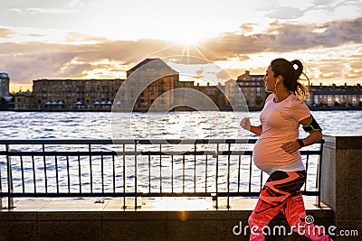 Pregnant woman running outside in a city at the riverside Stock Photo