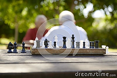 Active retired people, two old friends playing chess at park Stock Photo