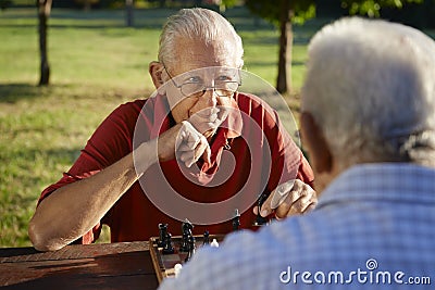 Active retired people, two senior men playing chess at park Stock Photo